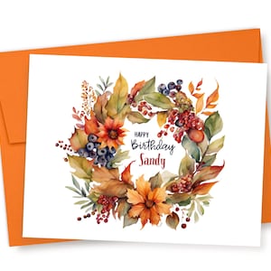 May include: A white card with a watercolor wreath of fall leaves, berries, and flowers. The text "Happy Birthday Sandy" is in the center of the wreath.