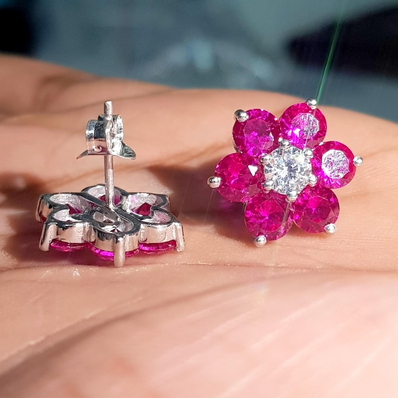 Peut inclure: Une paire de boucles d'oreilles &agrave; clous en forme de fleur. Chaque boucle d'oreille pr&eacute;sente six pierres pr&eacute;cieuses magenta autour d'une pierre centrale transparente. Les boucles d'oreilles sont serties dans un m&eacute;tal argent&eacute;.