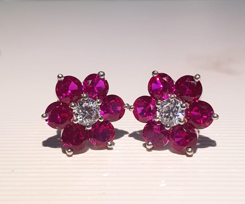 Peut inclure: Une paire de boucles d'oreilles &agrave; clous en forme de fleur. Chaque boucle d'oreille pr&eacute;sente une pierre centrale ronde et transparente entour&eacute;e de cinq pierres de couleur magenta. Les boucles d'oreilles sont serties dans un m&eacute;tal argent&eacute;.