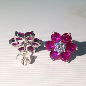 Peut inclure: Une paire de boucles d'oreilles &agrave; clous en forme de fleur. Chaque boucle d'oreille pr&eacute;sente un sertissage en m&eacute;tal argent&eacute; avec six pierres pr&eacute;cieuses magenta dispos&eacute;es en forme de p&eacute;tales. Un diamant clair et rond est au centre de chaque fleur.