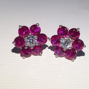 Peut inclure: Une paire de boucles d'oreilles &agrave; clous en forme de fleur. Chaque boucle d'oreille pr&eacute;sente six pierres pr&eacute;cieuses magenta entourant une pierre centrale transparente. Les boucles d'oreilles sont serties dans un m&eacute;tal argent&eacute;.