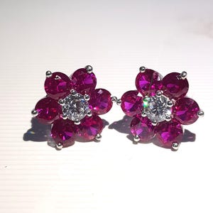 Peut inclure: Une paire de boucles d'oreilles &agrave; clous en forme de fleur. Chaque boucle d'oreille pr&eacute;sente une pierre centrale claire de taille ronde, entour&eacute;e de six petites pierres rose fonc&eacute;. Les boucles d'oreilles ont des tiges et des montures argent&eacute;es, cr&eacute;ant un design &eacute;l&eacute;gant et &eacute;tincelant.