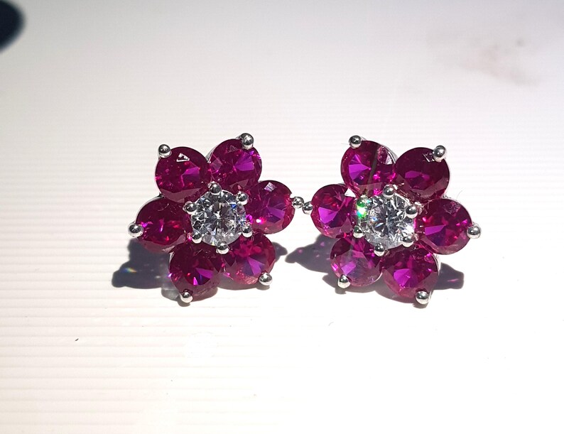 Peut inclure: Une paire de boucles d'oreilles &agrave; clous en forme de fleur. Chaque boucle d'oreille pr&eacute;sente une pierre centrale claire de taille ronde, entour&eacute;e de six petites pierres rose fonc&eacute;. Les boucles d'oreilles ont des tiges et des montures argent&eacute;es, cr&eacute;ant un design &eacute;l&eacute;gant et &eacute;tincelant.