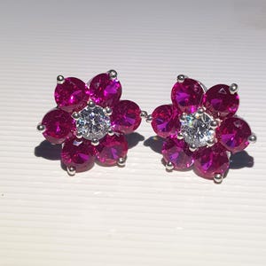 Peut inclure: Une paire de boucles d'oreilles &agrave; clous en forme de fleur. Chaque boucle d'oreille pr&eacute;sente six pierres pr&eacute;cieuses magenta entourant une pierre centrale transparente. Les boucles sont en m&eacute;tal argent&eacute;.