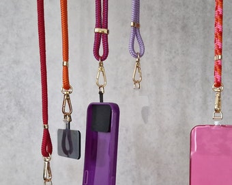 May include: Five phone straps with different colored cords and phone cases. The phone cases are purple, pink, and clear. The cords are red, orange, purple, and pink.