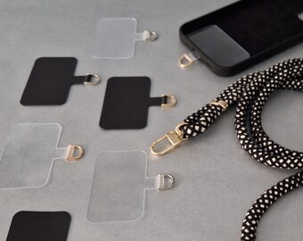 May include: A black and white phone strap with a black phone case and clear adhesive phone grips. The strap has white tassels on each end.