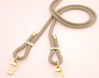 May include: A beige rope phone strap with gold hardware and the word "KISMET" engraved on the hardware.