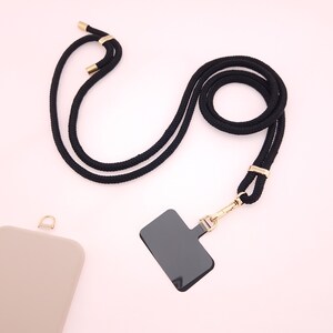 May include: Black phone strap with a gold clasp and a black rectangle phone holder. The strap is made of a thick, braided cord.