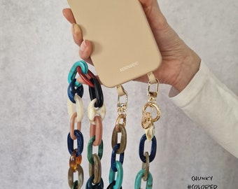 May include: Three colorful chunky phone straps with gold hardware. The straps are made of thick, colorful plastic links. The straps are attached to a beige phone case with the word "keewee" printed on the back.