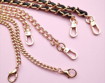 May include: Four gold chains with lobster clasps. The chains are of different lengths and thicknesses. The chains are on a pink background.