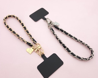 May include: Two black leather chain phone straps with gold and silver hardware. One strap has a heart charm with a sun design. Both straps have black rectangular tags.
