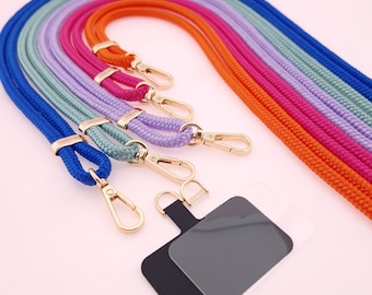 May include: A collection of colorful phone lanyards in blue, purple, pink, orange, and green. Each lanyard is made of a braided cord and features gold-colored metal clasps and connectors. A black and gray phone holder is also included.
