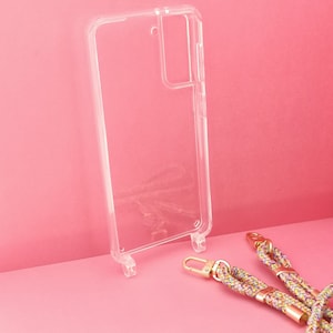 Pu&ograve; includere: Una custodia per telefono trasparente con un rialzo per la fotocamera e un cinturino per telefono intrecciato colorato con accessori dorati.