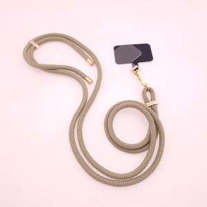 May include: A beige rope phone strap with gold hardware and a black and gray camera lens filter attached.