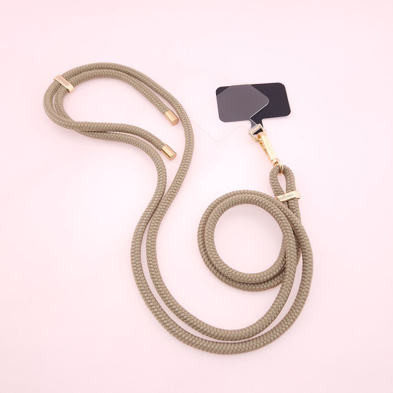 May include: A beige rope phone strap with gold hardware and a black and gray camera lens filter attached.