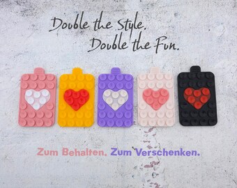 May include: Five colorful phone grips with heart designs. The grips are pink, yellow, purple, light pink, and black. The text "Double the style. Double the Fun." is above the grips.