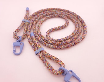 May include: A multi-colored braided rope leash featuring a vibrant pattern of orange, yellow, blue, and purple threads. The leash includes two light purple metal carabiner clips and matching light purple sliding adjustment rings.