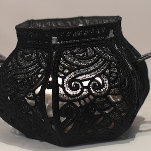 May include: Black lace candle lantern with a decorative design. The lantern has two handles and is made of a delicate, intricate lace pattern.