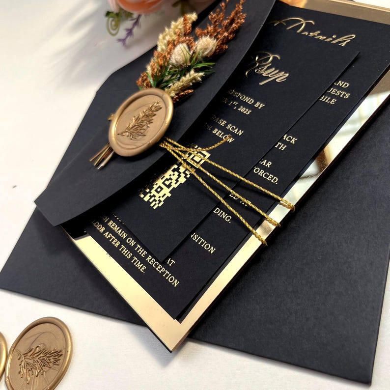 K&ouml;nnte beinhalten: Schwarze und goldene Hochzeitseinladung mit einem Wachssiegel und einem QR-Code. Die Einladung ist gefaltet und mit goldener Schleife gebunden. Der Text auf der Einladung lautet "Bitte bis zum 17.01.2025 antworten" und "Bitte unten scannen".