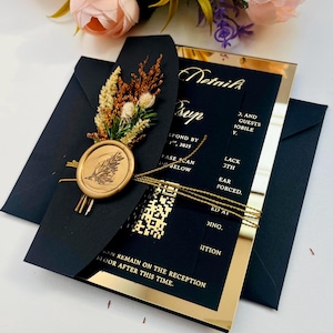 K&ouml;nnte beinhalten: Schwarze und goldene Hochzeitseinladung mit einem goldenen Siegel aus Wachs und getrockneten Blumen. Die Einladung hat eine goldene Spiegeloptik und der Text "Details sup" ist in Gold gedruckt.