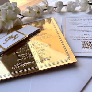 K&ouml;nnte beinhalten: Goldene Spiegel-Hochzeitseinladung mit wei&szlig;er Beschriftung. Die Einladung lautet "Save the Date" und enth&auml;lt Datum, Uhrzeit und Ort der Hochzeit. Die Einladung enth&auml;lt auch einen QR-Code f&uuml;r die RSVP.
