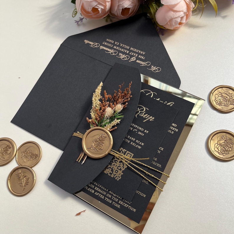 K&ouml;nnte beinhalten: Schwarze und goldene Hochzeitseinladung mit einem Wachssiegel und getrockneten Blumen. Die Einladung befindet sich auf einer verspiegelten Oberfl&auml;che. Der Text auf der Einladung lautet "Rsup" und "Bitte bis zum 1. Oktober 2021 antworten".
