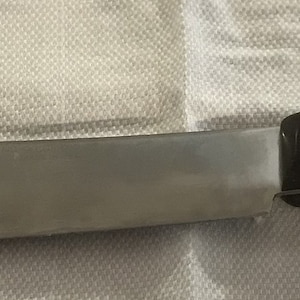 May include: A stainless steel kitchen knife with a black handle. The handle has a textured design and two white rivets.