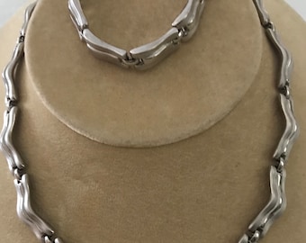 May include: A silver necklace and bracelet set with a wavy, linked chain design.
