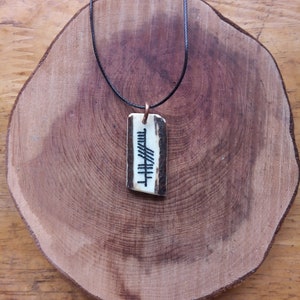 Op de afbeelding: Een zwarte koordsnoer met een hanger gemaakt van een stuk bot met een gegraveerd zwart-wit symbool.