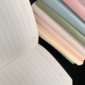 Peut inclure: Une pile de six cahiers vierges avec des couvertures de diff&eacute;rentes couleurs. Les couvertures sont rose, bleu clair, vert, rose clair, cr&egrave;me et bleu clair. Les cahiers ont un int&eacute;rieur lign&eacute; et un espace pour la date en bas de chaque page. Les cahiers sont parfaits pour tenir un journal, prendre des notes ou faire des croquis.