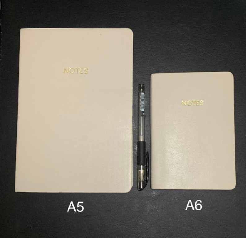 Peut inclure: Deux carnets beiges avec le mot "NOTES" imprim&eacute; en or sur le devant. Le carnet de gauche est &eacute;tiquet&eacute; "A5" et le carnet de droite est &eacute;tiquet&eacute; "A6".