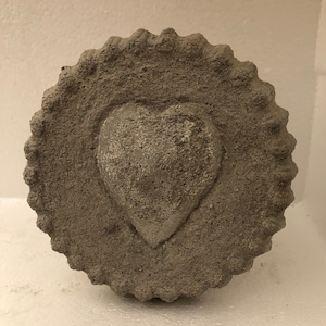 Puede incluir: Un adorno de corazón de hormigón gris con una superficie texturizada.