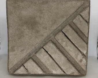May include: A square concrete tile with a geometric pattern of raised lines. The tile is a light gray color and has a rough texture.