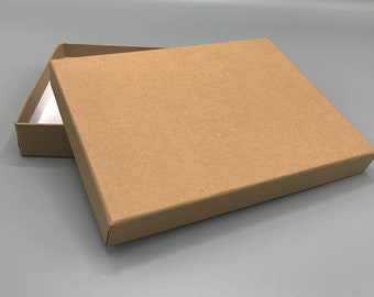 Puede incluir: Una caja de cartón marrón con tapa. La caja está abierta y la tapa está apoyada en la parte superior de la caja.