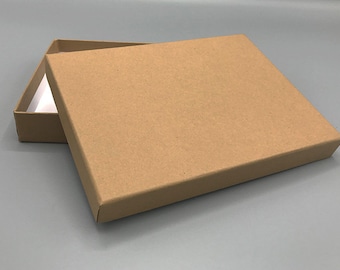 Puede incluir: Una caja de cartón marrón con tapa. La caja está abierta y la tapa está apoyada en la parte superior de la caja.