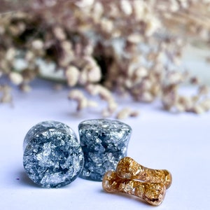 May include: Two round silver and black ear gauges with a pair of gold and black ear gauges.