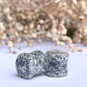 May include: Two silver and black ear gauges with a speckled, glittery finish.