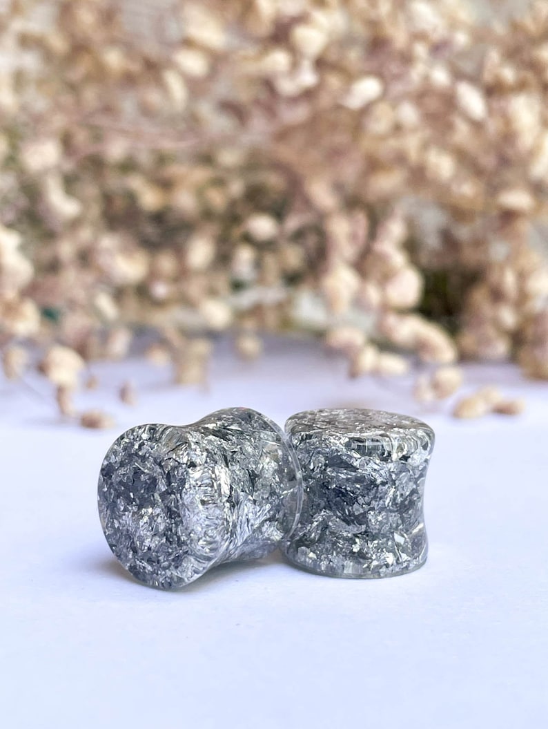 May include: Two silver and black ear gauges with a speckled, glittery finish.