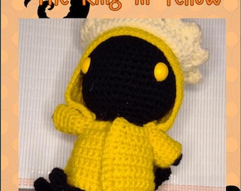 May include: A crocheted plush toy of Hastur, the King in Yellow, wearing a yellow raincoat and a white crown. The toy has black eyes with yellow pupils and a black body.