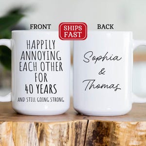 May include: White ceramic coffee mug with black text that reads "Happily annoying each other for 40 years and still going strong". The back of the mug has the names "Sophia & Thomas" written in black cursive.