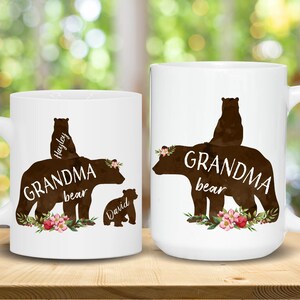 May include: Two white ceramic mugs with black bear silhouettes and floral accents. The text on the mugs reads "Grandma bear" with the names "Hayley" and "David" on the smaller bears.
