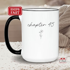 May include: White ceramic mug with a black handle and rim. The mug features the text "chapter 45" in a script font, along with a small floral illustration. The mug is a standard size for coffee or tea.
