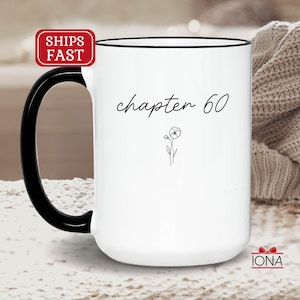 May include: White ceramic mug with a black handle and rim. The mug features the text "chapter 60" in a handwritten font, along with a small floral illustration. A red and white "SHIPS FAST" sticker is visible on the top left.