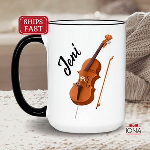 May include: White ceramic mug with a black handle and rim. The mug features a cartoon illustration of a cello and bow with the name "Jeni" written in black cursive.