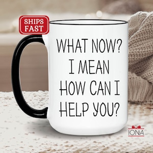 May include: White ceramic mug with a black handle and rim. The mug features the text "WHAT NOW? I MEAN HOW CAN I HELP YOU?" in black. A red and white "SHIPS FAST" sticker is visible on the top left. The mug is next to a beige knitted item.