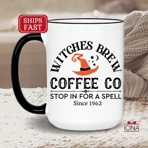May include: White ceramic mug with a black handle and rim. The mug features the text "Witches Brew Coffee Co" with a witch hat and stars graphic. The text "Stop in for a spell Since 1962" is also printed on the mug.