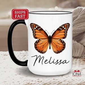 May include: White ceramic coffee mug with a black handle and rim. The mug features a colorful butterfly illustration and the name "Melissa" in black cursive writing.