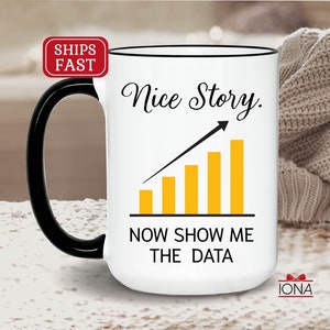 May include: White ceramic coffee mug with a black handle. The mug has a black rim and a graphic of a yellow bar chart with an upward arrow and the text "Nice Story. Now Show Me The Data".