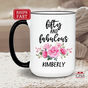 May include: White ceramic mug with a black handle and rim. The mug has a black and pink floral design with the text "fifty and fabulous KIMBERLY".