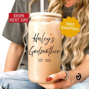 May include: A clear glass tumbler with a lid and a straw. The tumbler has a brown liquid inside and black text that reads "Haley's Godmother Est. 2025".